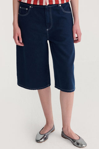Woman dark denim bermuda shorts with contrast stitching and silver ballet flats. 