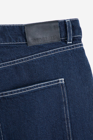 Close-up of back waistband of dark blue denim bermuda shorts with white contrast stitching. 