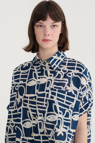 Woman wearing button up short sleeve top with navy blue and cream abstract print. 