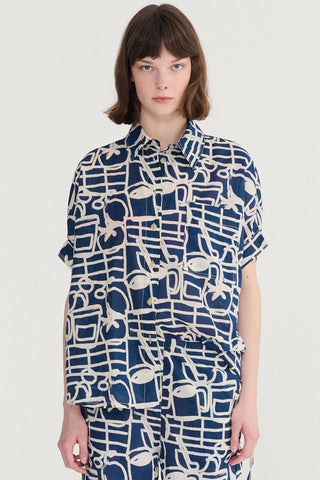 Woman wearing button up short sleeve top and pants with navy blue and cream abstract print. 