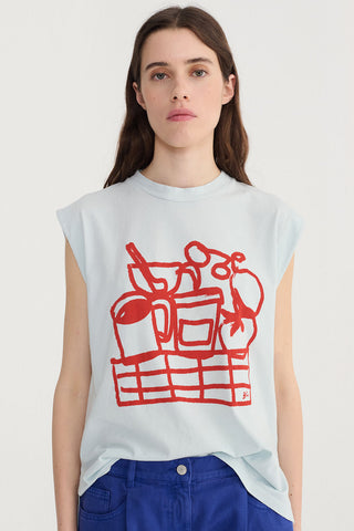 Woman wearing light blue tank top with bold red food-inspired print. 