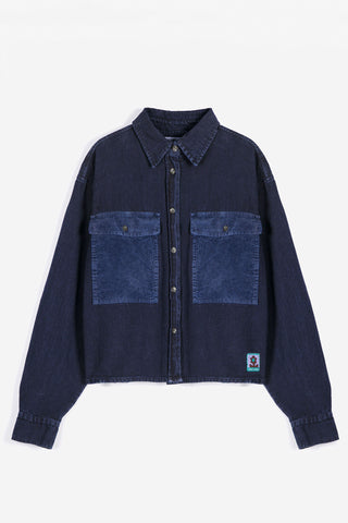 A dark indigo denim shirt with contrasting medium blue corduroy chest pockets, shown flat against a light gray background.