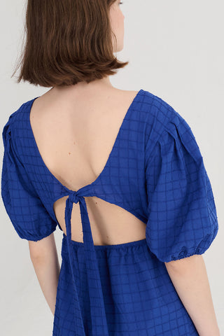 Woman wearing a blue dress with balloon sleeves and open back. 