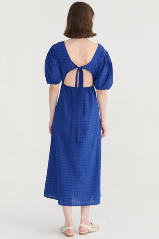 Woman wearing a cobalt blue midi length dress with balloon sleeves and open back. 