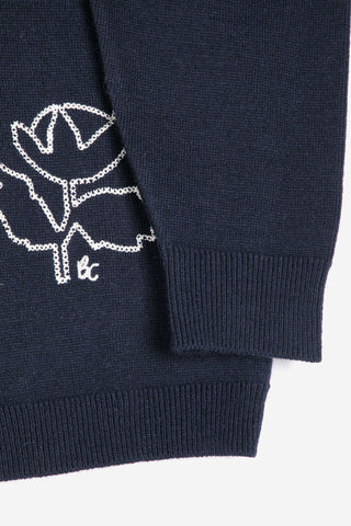 Close-up of a navy knit garment with a white embroidered flower motif and a small 'B&C' logo near the cuff.