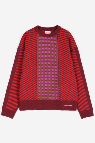 A red and magenta knit sweater with diagonal striped sleeves and a central checkerboard pattern panel, shown flat on a light gray background.