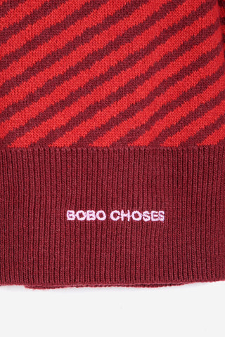 Close-up of a ribbed knit sweater in red and dark burgundy with diagonal stripes, with the text 'BOBO CHOSES' embroidered in light pink.