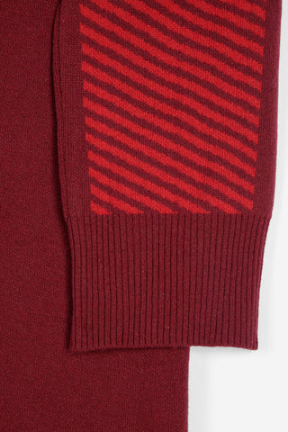 Close-up of a knit garment showing a ribbed cuff in deep burgundy with a contrasting panel of diagonal red and burgundy stripes.