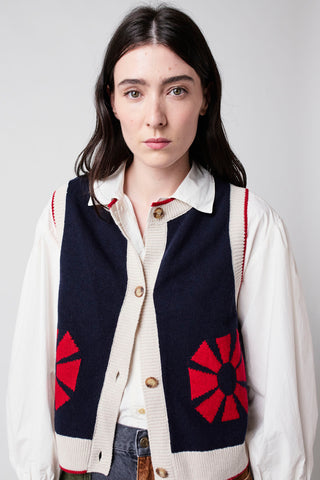 Model wearing navy sleeveless button up knit vest with red geometric flower and cream trim by Bobo Choses, over white shirt. 