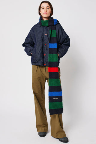 Woman wearing pinstripe denim jacket, olive pants, and multi colour stripe scarf by Bobo Choses. 