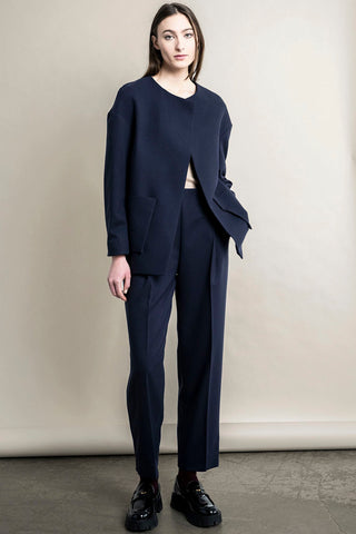 Woman standing in front of beige background, wearing navy Regent Blazer and matching pants by Bodybag. 