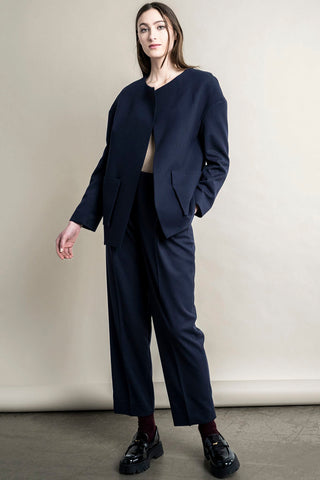 Woman standing in front of beige background, wearing navy Regent Blazer and matching pants by Bodybag. 