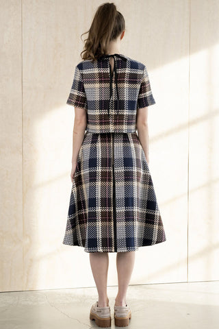 A woman viewed from behind wearing a short-sleeve plaid top and matching A-line skirt in brown plaid. 