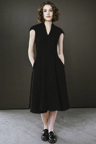 Woman in front of dark coloured wall wearing black tweed v-neck midi length Highland dress by Bodybag. 