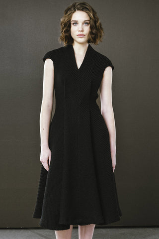 Woman in front of dark coloured wall wearing black tweed v-neck midi length Highland dress by Bodybag. 
