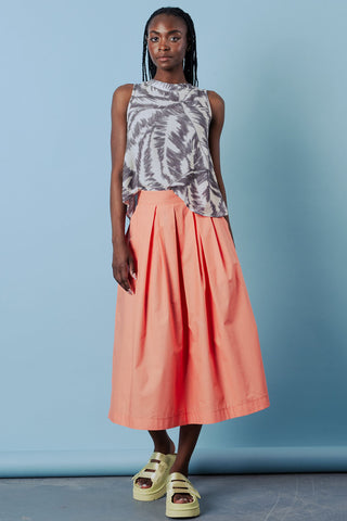 Woman wearing a sleeveless patterned top and coral skirt against a blue background