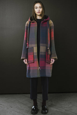 Woman standing in front of dark wall, wearing navy and red plaid zip up Morrison Coat by BodyBag. 