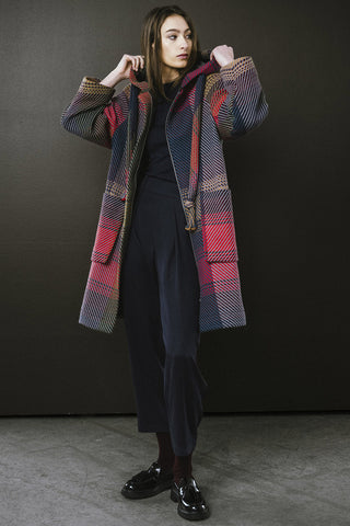 Woman standing in front of dark wall, wearing navy and red plaid unzipped Morrison Coat by BodyBag. 