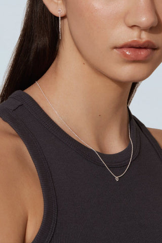 Close-up of woman wearing black tank top and delicate silver chain with tiny circle pendant. 