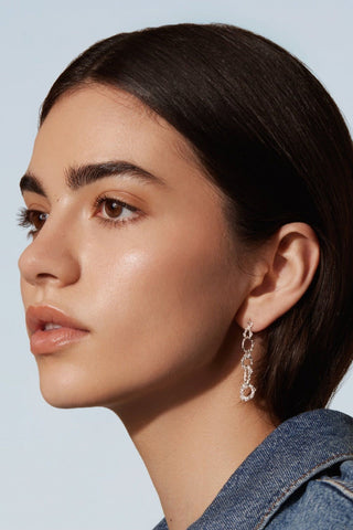 A side profile of a woman's face wearing sterling silver chunky chain drop earrings by Camillette. 
