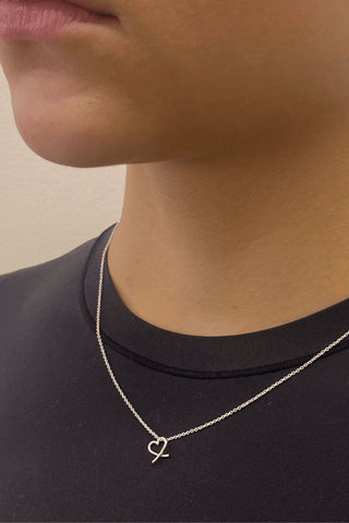 Close-up of model wearing black t-shirt and delicate sterling silver chain with heart pendant. 