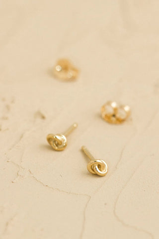 Gold knot earrings on a beige marble surface