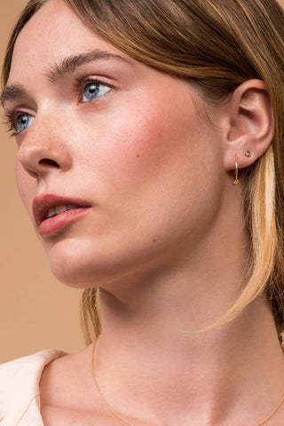 Close-up of a woman's face wearing a hoop earring and gold knot earring stud. 