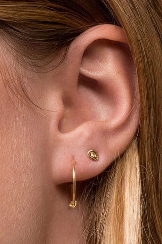 Close-up of a woman's ear wearing a hoop earring and gold knot earring stud. 