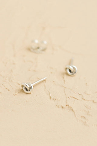 Knot shaped silver stud earrings on a beige marble surface.