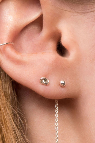 Close-up of a woman's ear wearing a danlge earring and silver knot earring stud. 