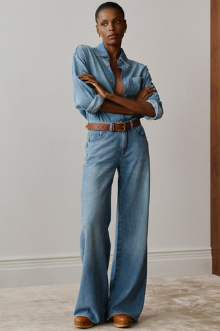 Woman in front of plain background wearing denim shirt with baggy wide leg jeans. 