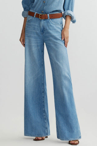 Woman in front of plain background wearing mid-blue wash baggy wide leg jeans with brown leather belt. 