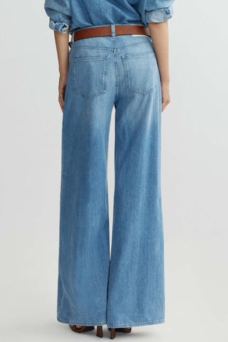 Back view of woman in front of plain background wearing mid-blue wash baggy wide leg jeans with brown leather belt. 