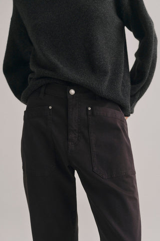 Close-up of a person wearing dark charcoal knit sweater and brown jeans with oversized front patch pockets, against a light gray studio background.