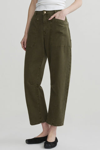 A person shown from waist down wearing olive green cropped barrel leg jeans with black flats, shown against a light gray studio background.