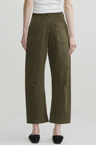 A person shown from the back, waist down, wearing white tank top and olive green cropped barrel leg jeans with black flats, shown against a light gray studio background.