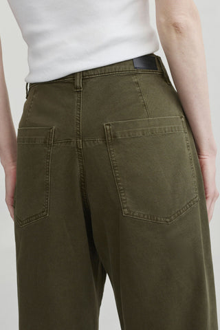 Close-up back view of a person wearing olive green barrel leg jeans with a white ribbed top, showing the back pockets and waistband.