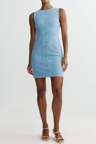 Woman wearing light blue fitted denim mini dress in front of white background. 