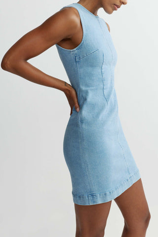 Woman wearing light blue fitted denim mini dress in front of white background. 