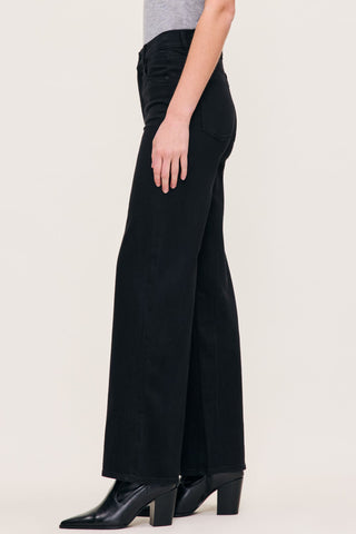 A model wearing black wide-leg jeans and black pointed-toe ankle boots, shown from the waist down against a plain light beige studio background.
