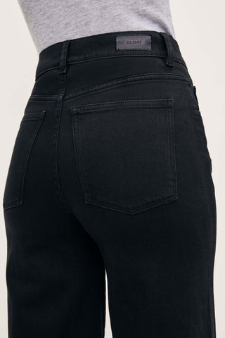 Close-up back view of a person wearing dark washed denim jeans with a gray top, showing the waistband, belt loops, and back pocket details. A small DL1961 label is visible at the back waist.