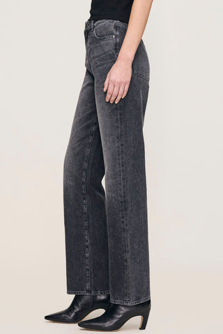 Side view of woman in front of plain background wearing black faded straight leg Karmine jeans by DL1961. 