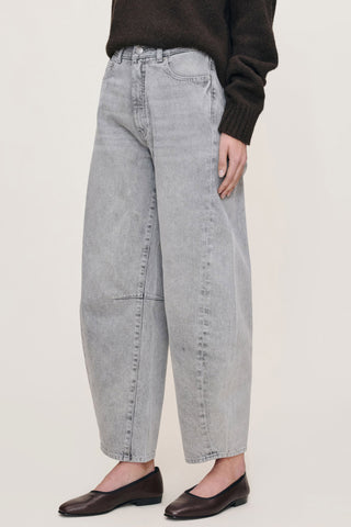 Women standing in front of white background wearing grey wash high waist barrel cut jeans. 