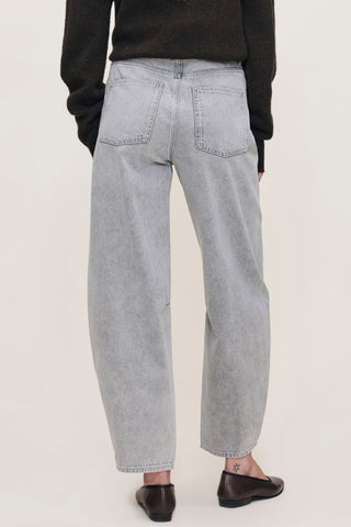 Back view of women standing in front of white background wearing grey wash high waist barrel cut jeans. 