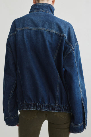A person shown from the back wearing a dark blue denim jacket with a gathered elastic hem and olive green pants, photographed against a plain light gray studio background.