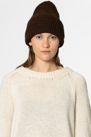 Woman in front of white background wearing ivory knit sweater and brown coloured alpaca wool handknit toque by Dinadi. 