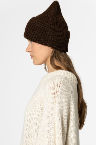 Side view of woman in front of white background wearing ivory knit sweater and brown coloured alpaca wool handknit toque by Dinadi. 