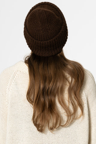 Back view of woman in front of white background wearing ivory knit sweater and brown coloured alpaca wool handknit toque by Dinadi. 