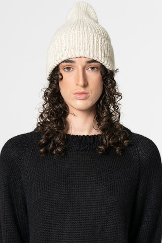 Woman in front of white background wearing black knit sweater and ivory coloured alpaca wool handknit toque by Dinadi. 