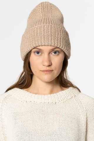 Woman wearing cream sweater and sand chunky knit toque, in front of white background. 